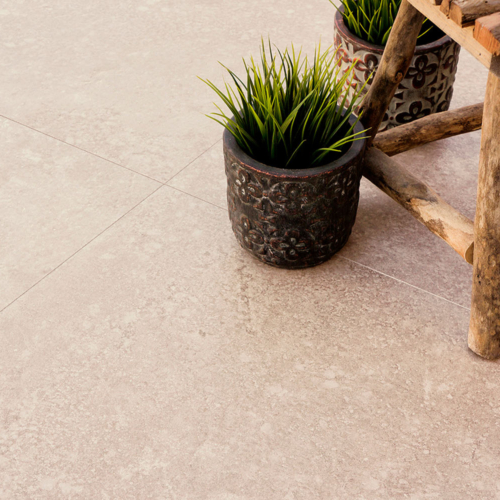 Rustikaler Holzstuhl auf beigem Boden mit zwei Pflanztöpfen und grünem Gras.
