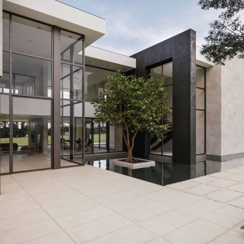 Modernes Haus mit Glasfenstern, Wasserbecken, Baum im Innenhof und teilweise sichtbarem Auto.