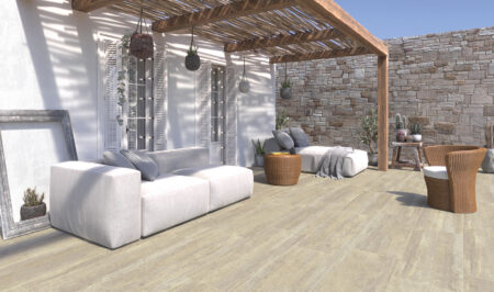 Terrasse mit weißen Sofas unter Holzpergola, Steinmauer, Kissen, Pflanzen, Dekorationen.