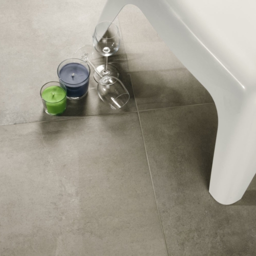 Weißer Stuhl auf grauem Fliesenboden, mit grüner und blauer Kerze, zwei umgekippte Weingläser.