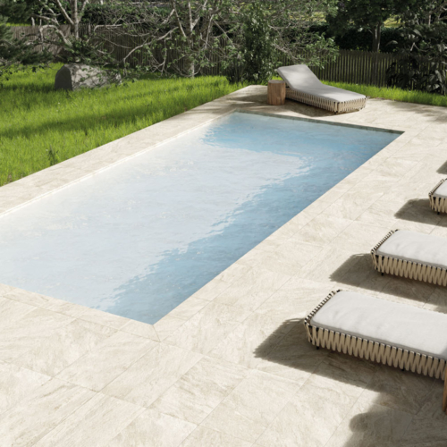 Rechteckiger Gartenpool mit beigen Fliesen, Holzliegen und grünem Rasen im Hintergrund.