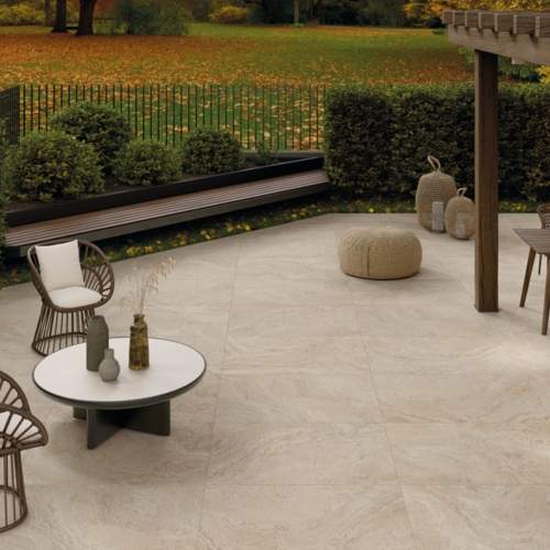 Moderner Terrassenbereich mit hellen Fliesen, geflochtenen Stühlen, Tischen und Herbstlaub.