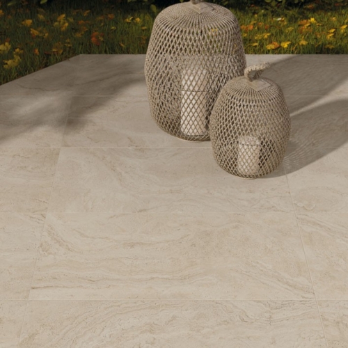 Zwei geflochtene Laternen mit Kerzen auf beiger Steinplatte, umgeben von grünem Laub.